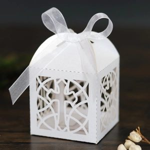 Close-up of white laser-cut cross gift box with elegant vine patterns and a silk ribbon