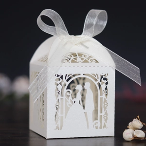 Detail of laser-cut white wedding favor box with bride and groom silhouette and ribbon