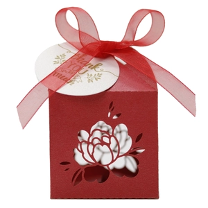 Macro detail of red laser-cut floral wedding favor box with ribbon and thank you tag