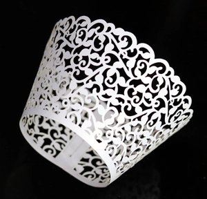 Detailed laser-cut white cupcake wrapper with elegant vine patterns on a black background
