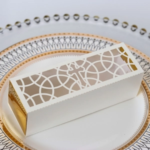 Detailed macro view of laser-cut hollow cross pattern on white and gold wedding favor box