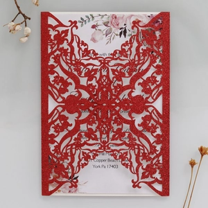Detail view of laser-cut wedding invitation with red glitter cover and elegant floral inner
