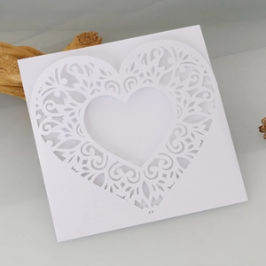 Macro shot of white laser-cut heart card with intricate vine patterns for weddings