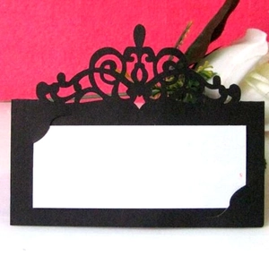 Close-up of black laser-cut place card with crown pattern and writing area on pink background