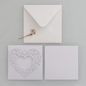 Macro view of white laser-cut hollow heart invitation with envelope and insert paper