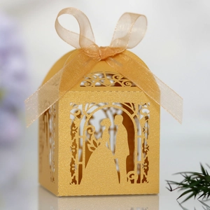 Close-up of golden laser-cut candy box with bride and groom silhouette and ribbon
