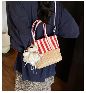 Detail view of striped canvas and straw tote bag with a plush dog charm on a model