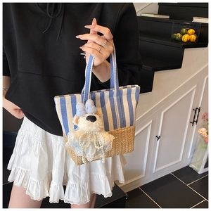 Detail of canvas stripe tote bag featuring a plush bear charm and woven straw base