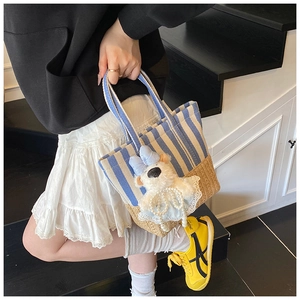 Close-up of blue and white striped tote bag with woven straw base and bear charm