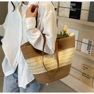 Detail of woven straw tote bag featuring contrast color stripes and leather handles