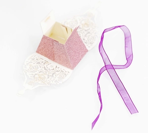 Detailed laser-cut hollow pattern on pink glitter favor box with purple ribbon