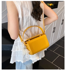 Detailed view of yellow faux leather box bag with pearl charm and lace bow accessory
