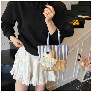 Close-up of blue striped canvas and woven straw bucket bag with cute bear pendant