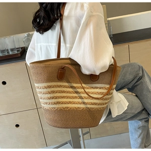Detail of a large straw tote bag with brown leather handles and striped woven texture