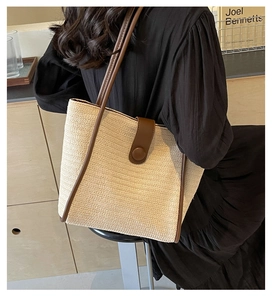 Detail of woven straw tote bag featuring brown faux leather trim and round buckle closure