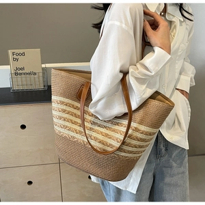 Detail of a large straw tote bag featuring brown leather straps and striped woven texture