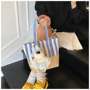 Detail of blue striped canvas and straw woven bucket bag with a cute plush bear charm