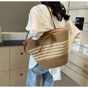 Detail of a large straw tote bag with brown leather straps and striped woven texture