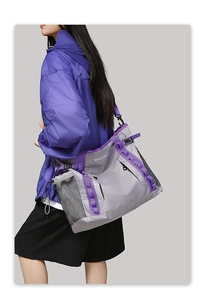Detail view of large grey travel bag with purple straps and mesh side pocket worn by model
