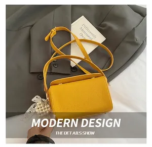 Detail of yellow lychee leather mini crossbody bag with pearl lace charm on grey suit
