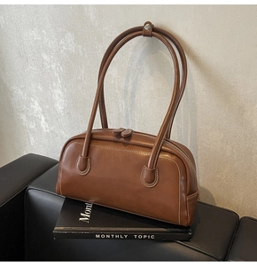 Detailed view of a brown leather shoulder bag with white contrast stitching and zip closure