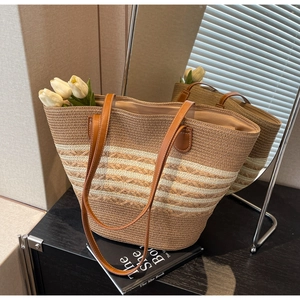 Detail of striped straw tote bag featuring brown faux leather handles and woven texture