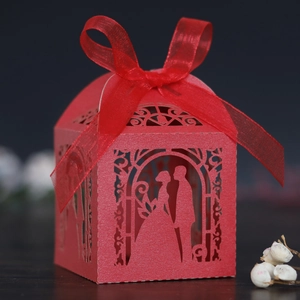 Detail of red laser-cut wedding favor box with bride and groom silhouette and ribbon