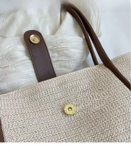 Detail view of woven tote bag with a golden magnetic buckle and brown leather strap