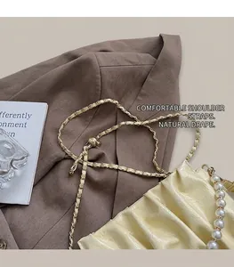 Détail du sac nuage plissé crème avec anse en perles et chaîne dorée sur un blazer
