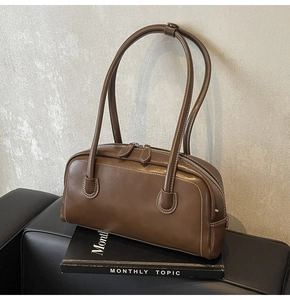 Detail of brown leather underarm bag with contrast white stitching and metal zippers