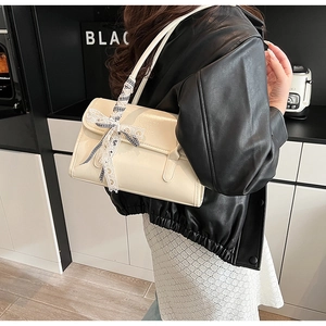 Close-up of a beige patent leather shoulder bag with a stylish black and white checkered bow