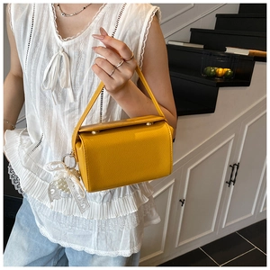 Detail of yellow pebbled leather crossbody bag with pearl and lace bow charm detail
