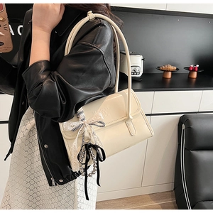 Detail of off-white shoulder bag with letter embossing, bow and pearl charms worn by model