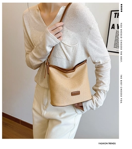 Detailed view of woven straw bucket bag with brown leather trim and shoulder strap