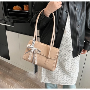 Detail of beige patent leather bag featuring a striped ribbon bow and embossed logo
