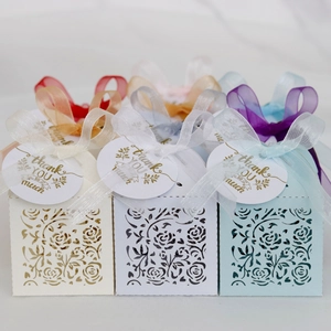 Macro detail of laser-cut floral wedding favor boxes with satin ribbons and thank you tags