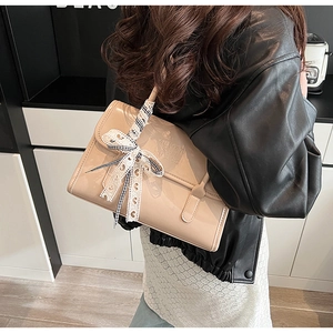 Detail of light beige patent leather bag with embossed logo and plaid ribbon bow