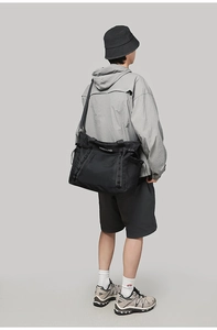 Rear view of a man carrying a large black waterproof nylon duffel bag for travel and fitness