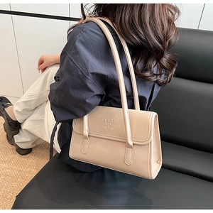 Model wearing a beige leather shoulder bag with embossed texture and double straps
