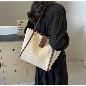 Detailed shoulder view of a woven tote bag with contrast leather trim and round buckle