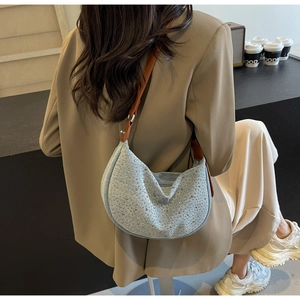 Detail of light blue denim hobo bag with rhinestones and brown leather strap on shoulder