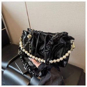 Detail of black patent leather bag with pleated texture and white pearl strap