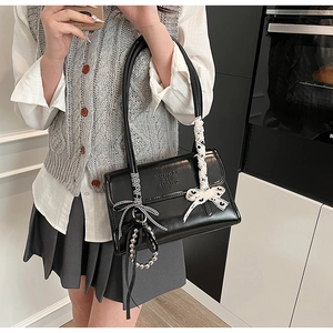 Detail of black faux leather shoulder bag featuring bow decor and embossed lettering