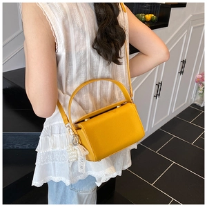 Detail view of a bright yellow pebble leather square handbag with pearl and bow accessories