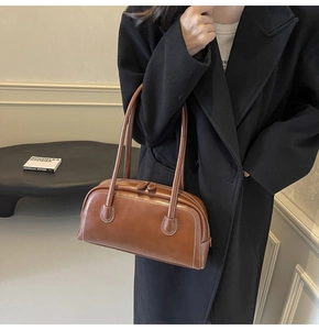 Close-up of brown leather Boston bag with decorative white stitching and double handles