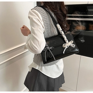 Detail of black underarm bag with lace bow and letter embossing in a modern setting
