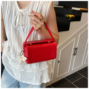 Detail of red litchi grain leather handbag with pearl strap and lace bow charm