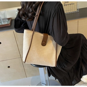 Close-up of beige woven tote bag featuring dark brown leather trim and round buckle detail