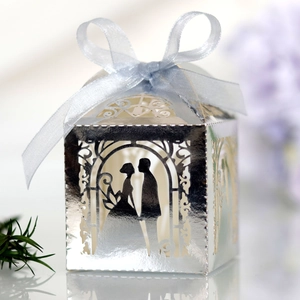 Detail of silver laser-cut wedding favor box with bride and groom silhouette and blue bow