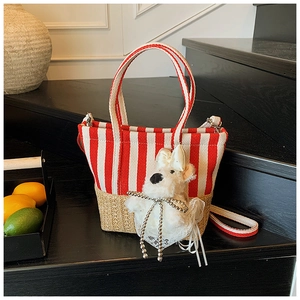 Detail of red stripe canvas tote with straw base and plush puppy charm on wooden steps